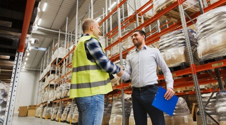 An image of two people shaking hands happily inside a warehouse.
