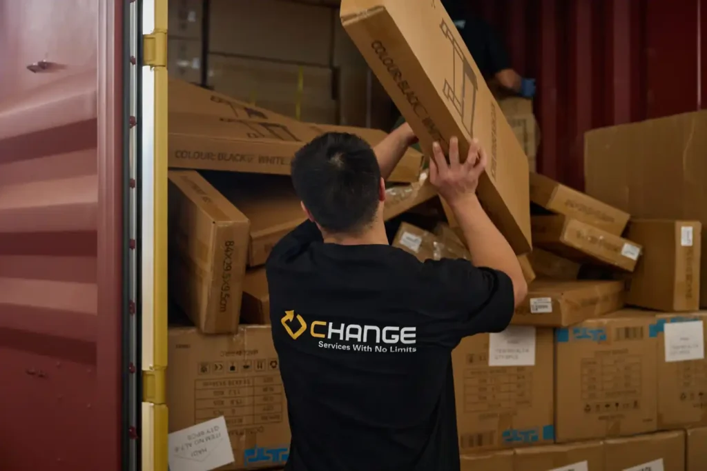 Change Sourcing worker loading large cartons into a shipping container, showing export shipment preparation and sourcing-stage checks for European market entry.